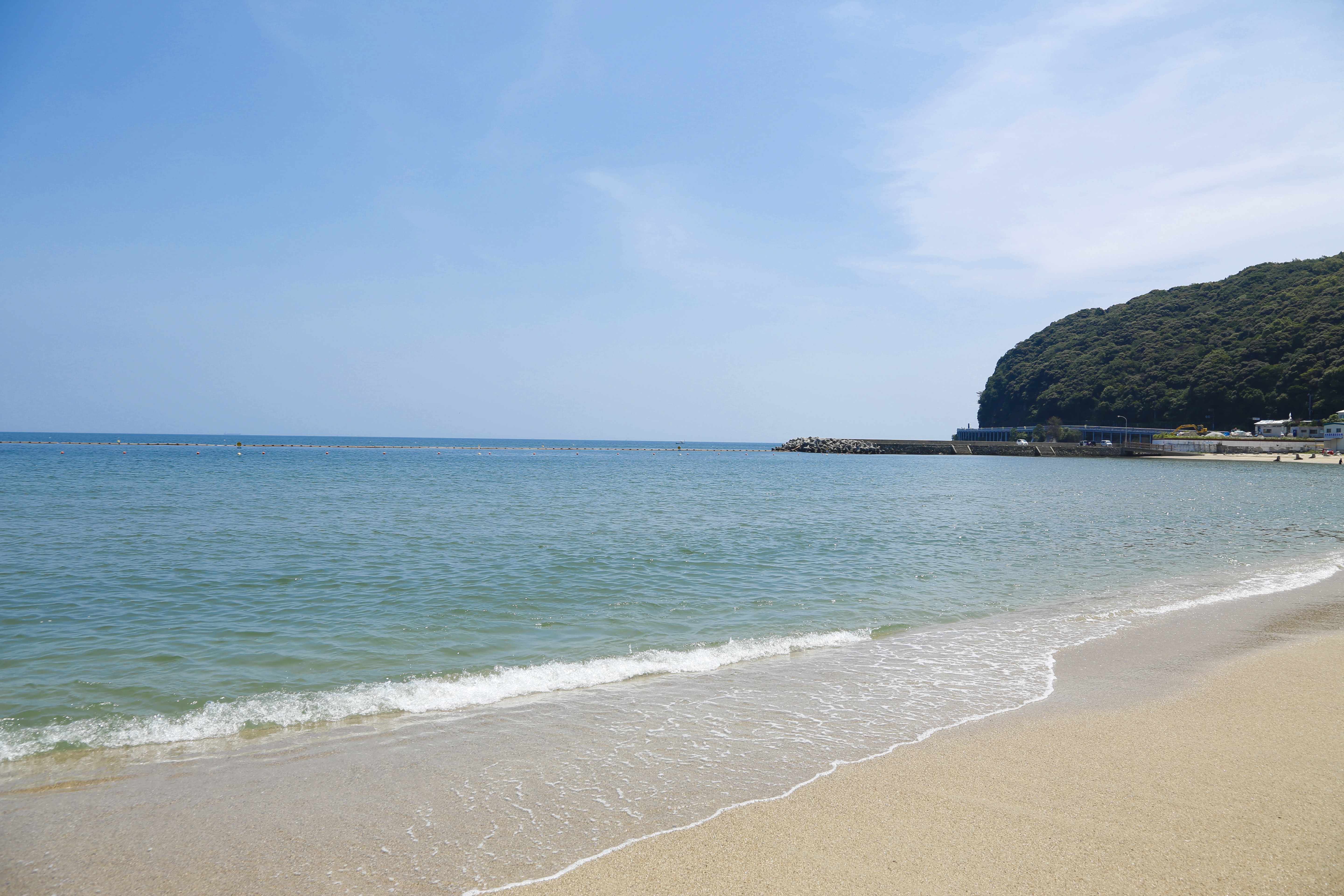 Calm sandy beach with clear turquoise water and a rocky coastal outcrop, evoking the natural coastal retreat at the heart of the Awaji Island experience