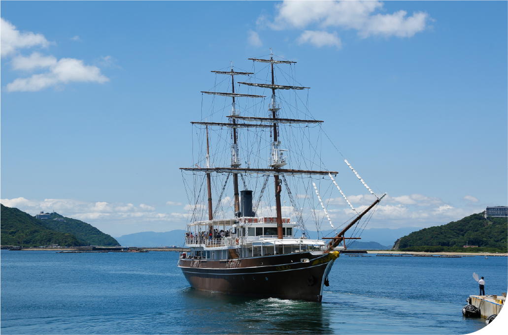 Tall-masted sailing vessel on calm waters surrounded by Awaji Island's forested hills, evoking a sense of open horizon and unhurried discovery