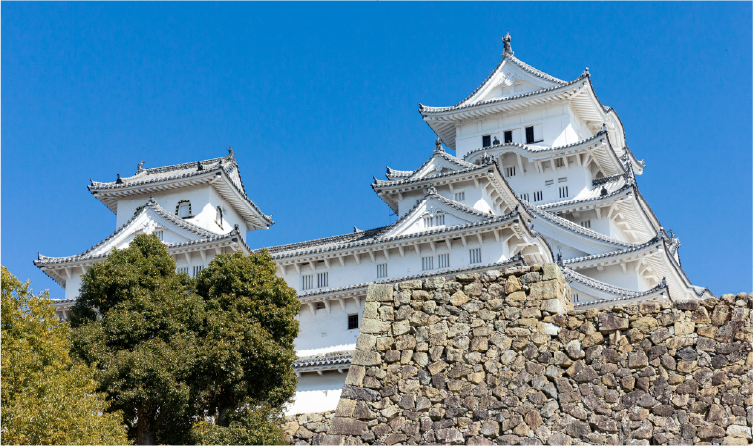 Historic white Himeji Castle with stone walls and blue sky, showcasing a UNESCO-listed landmark accessible from Kobe