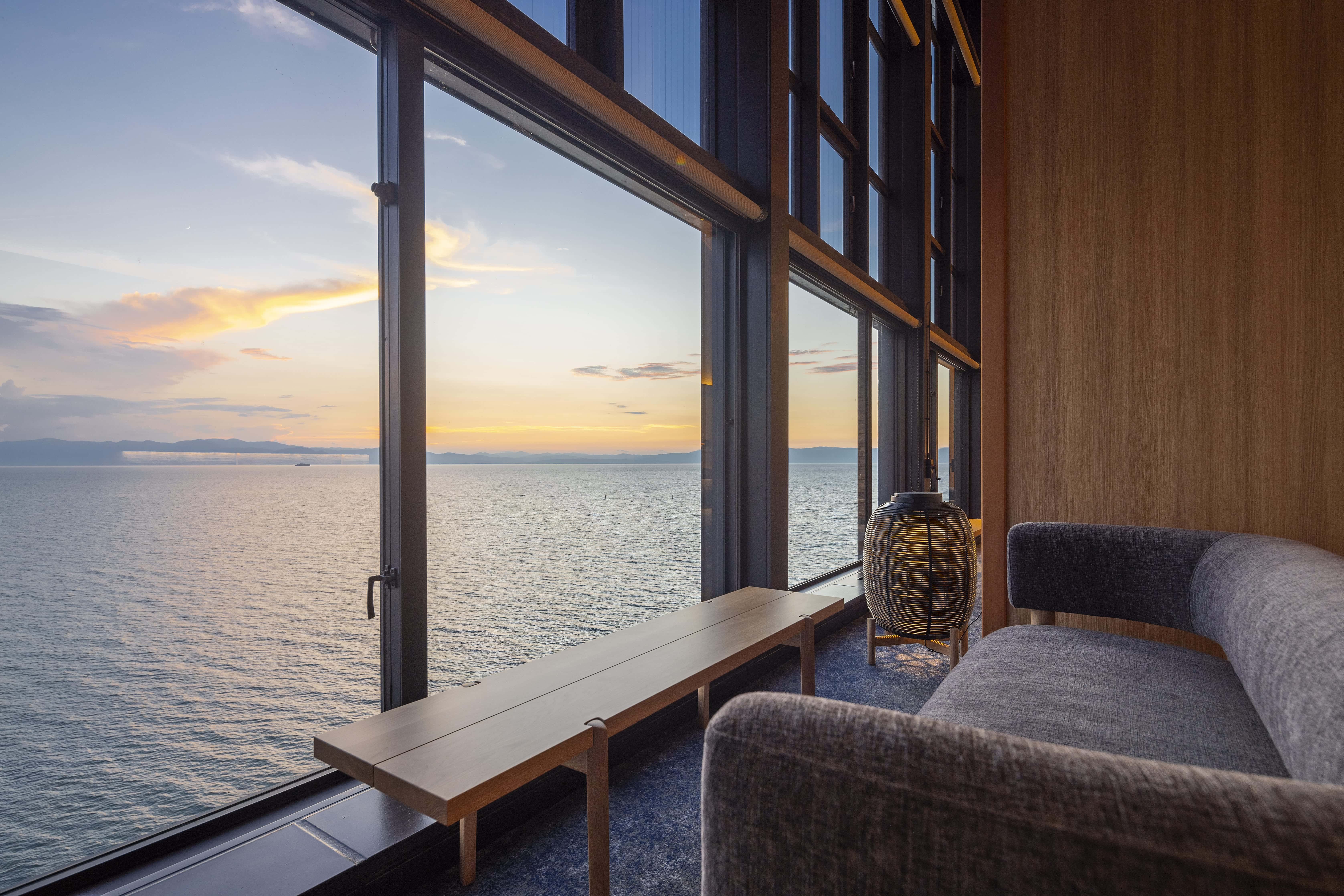 Guest room lounge overlooking Lake Biwa at sunset with panoramic windows, luxury hotel in Shiga Japan