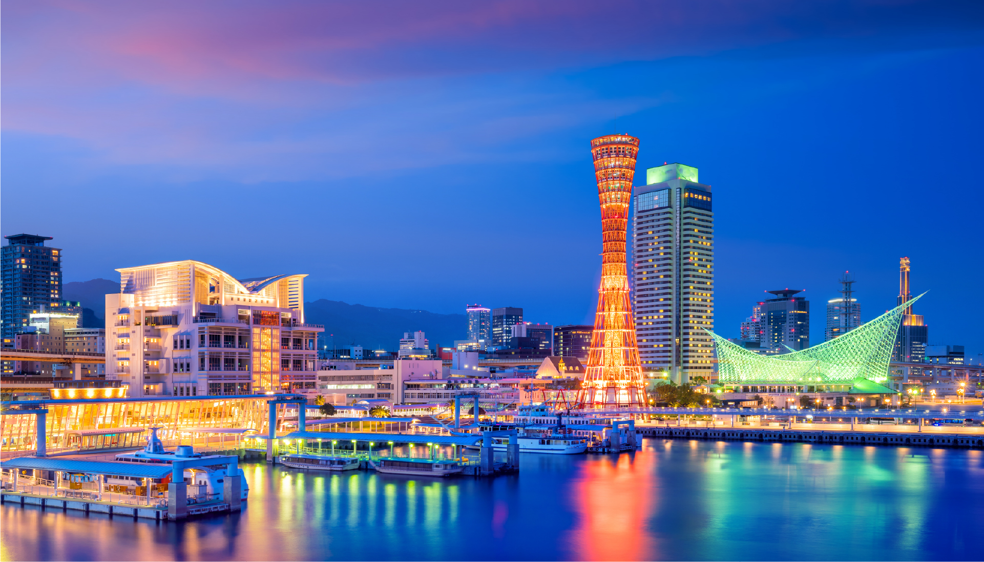 Kobe harbor skyline at night with Kobe Port Tower glowing in red and orange, its reflection shimmering across the water in a city where sea, light, and modernity converge