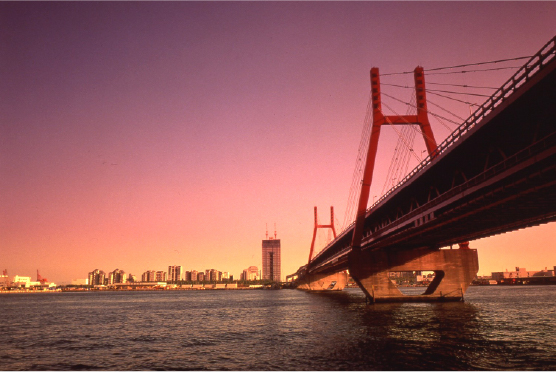 Bridge at golden hour with a warm pink sky reflected on calm harbor waters, an iconic symbol of Kobe's coastal ambition and engineering craft