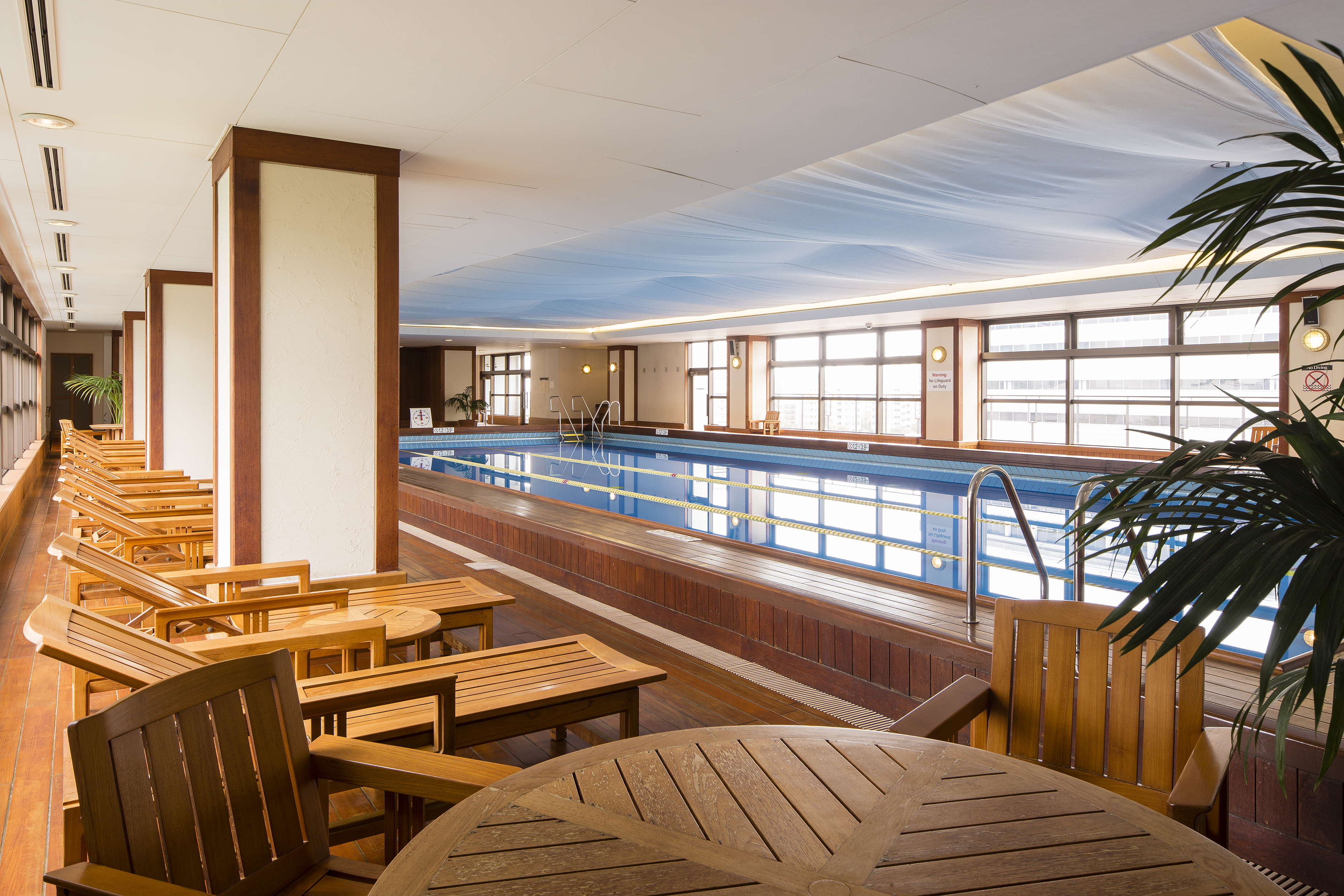 Indoor lap pool with large windows and wooden deck at Kobe Bay Sheraton, part of Hotel New Awaji Group, where natural light and calm water create an inviting space for quiet recreation