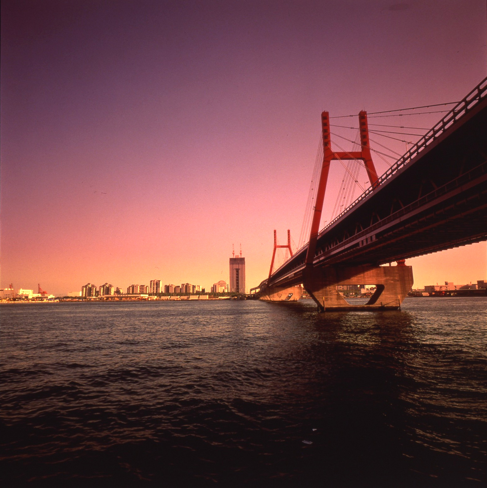 Bridge rising dramatically against a deep pink and purple sunset sky viewed from the water, one of Kobe's most powerful and iconic coastal perspectives