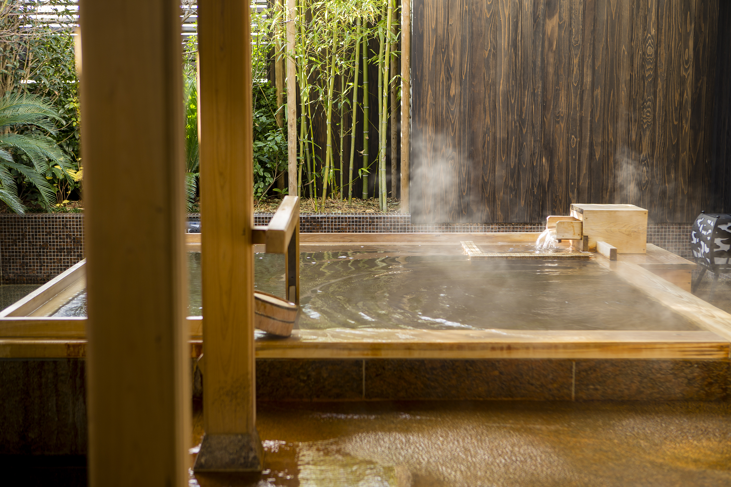 Steaming onsen bath enclosed by tall bamboo at Kobe Bay Sheraton, part of Hotel New Awaji Group, where rising mist and lush greenery create a deeply restorative urban wellness retreat