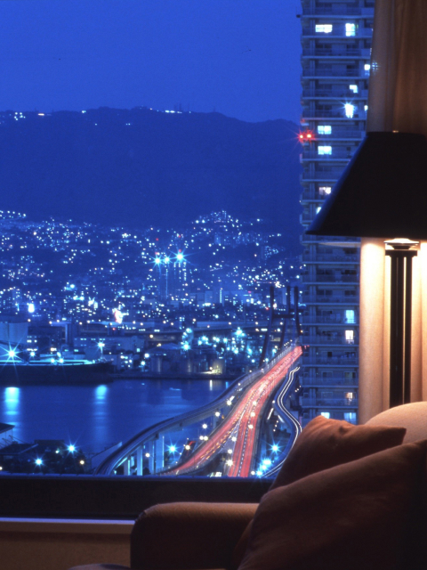 Floor-to-ceiling window view of Kobe's glittering city lights at night from a high-floor guest room at Kobe Bay Sheraton, part of Hotel New Awaji Group, where the city becomes part of the stay