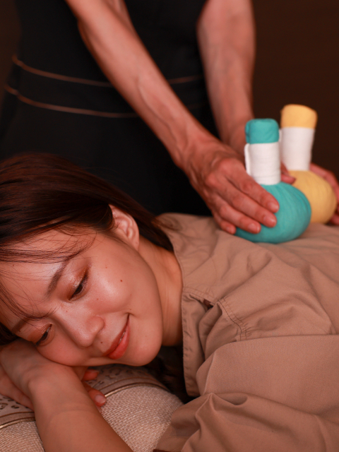 Therapist applying a warm herbal compress massage to a guest at Kobe Bay Sheraton, part of Hotel New Awaji Group, delivering a deeply restorative and sensory wellness experience