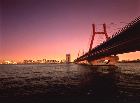 Bridge illuminated at golden hour over Kobe's calm harbor waters, a landmark symbol of the city's modern ambition and coastal character