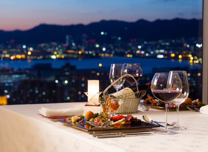 Candlelit dining table with wine and seasonal dishes overlooking Kobe's glittering city lights, combining refined hospitality with an unforgettable urban view