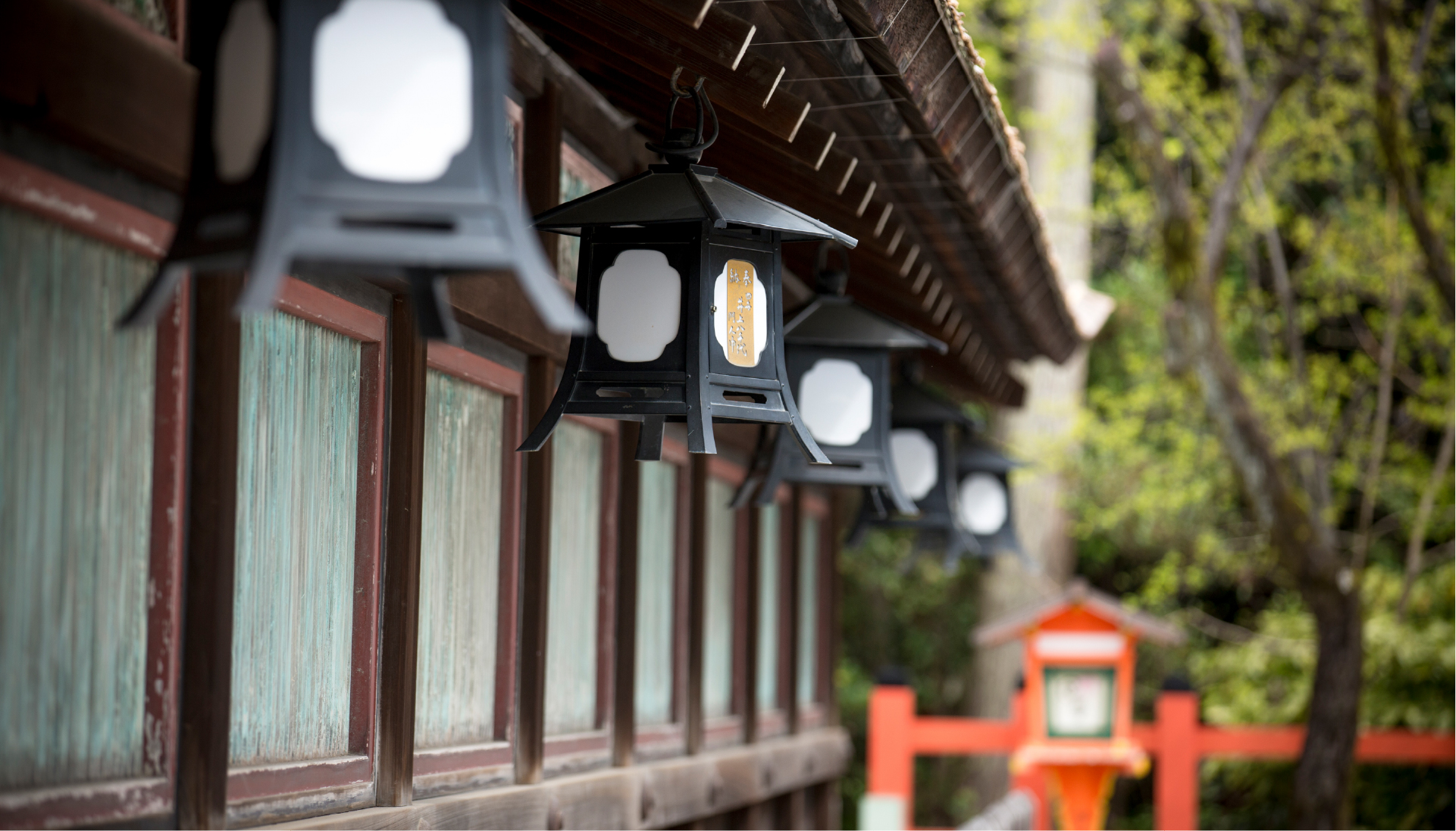 Traditional black lanterns lining a vermillion shrine corridor in Kyoto, where centuries of ritual and architectural craft meet living tradition
