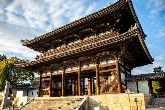 Grand wooden temple gate with golden ornamentation rising under a clear Kyoto sky, a testament to centuries of architectural devotion and craft