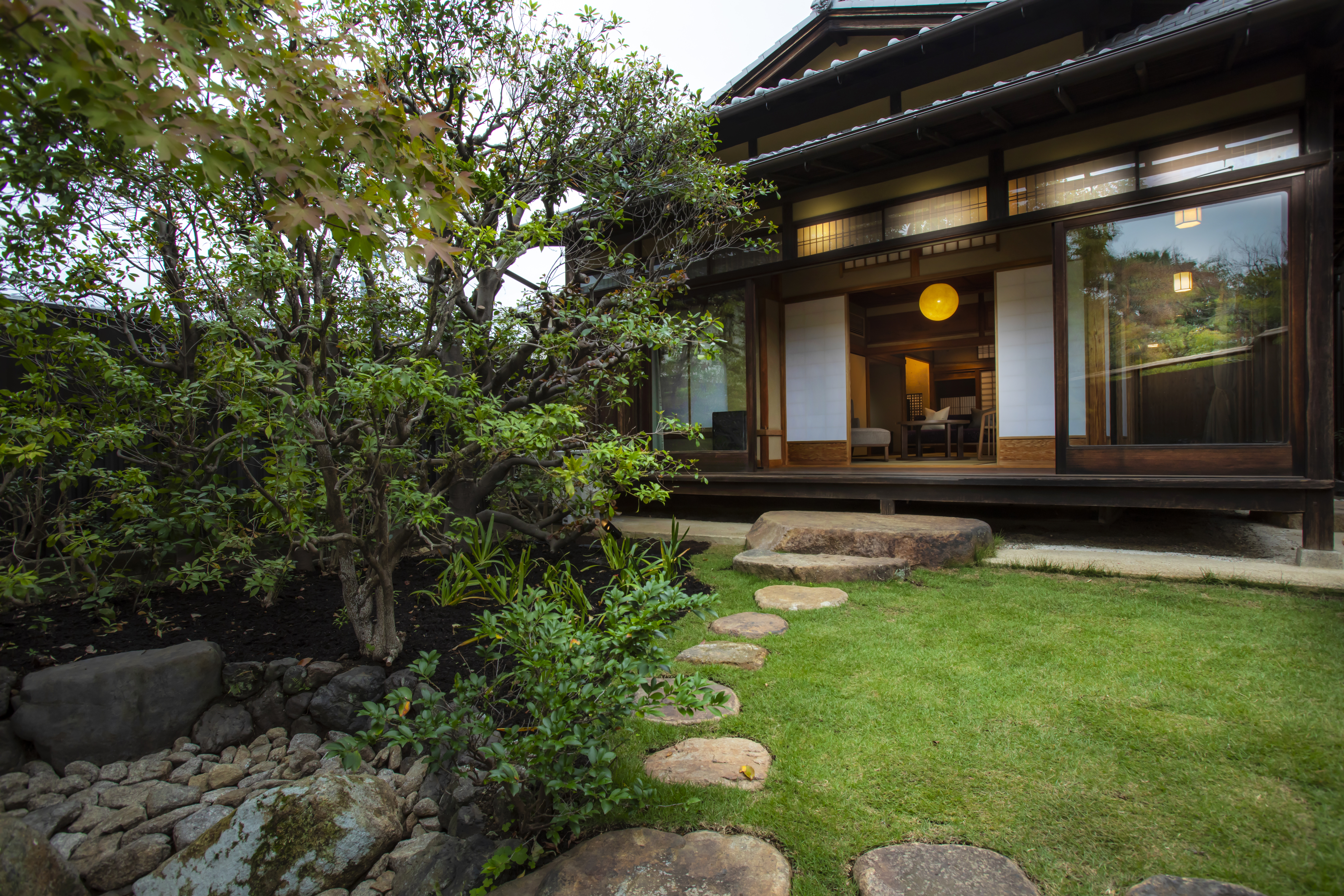 Stepping stone path leading to a traditional ryokan entrance surrounded by manicured greenery, inviting arrival and calm