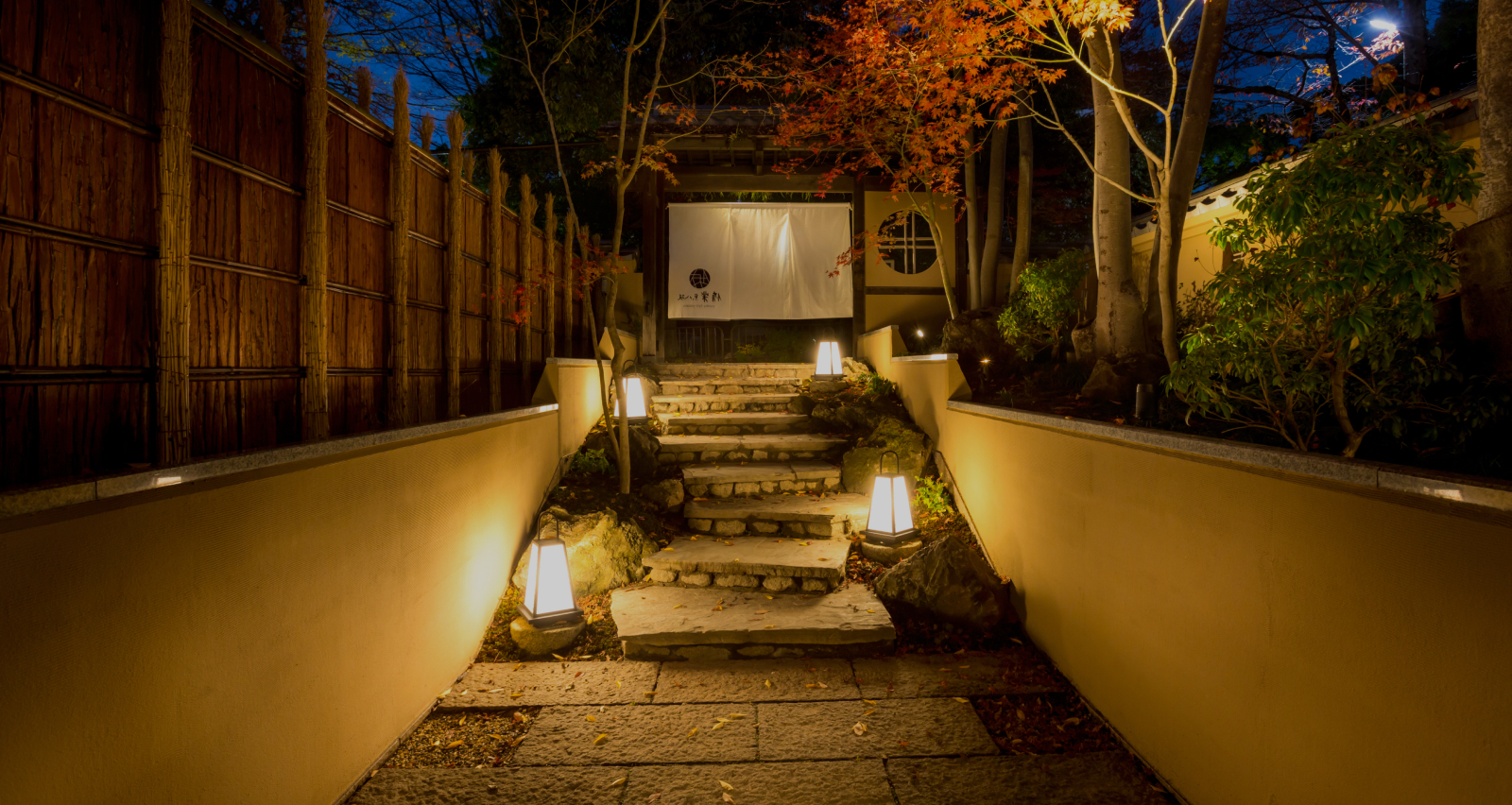 Hotel New Awaji Group Kyoto property warmly illuminated at night amid autumn foliage, offering a refined and atmospheric arrival in Japan's cultural capital