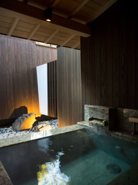 Stone-bed private onsen bath with natural rock detailing and ambient lighting, offering a deeply restorative and atmospheric soak at Hotel New Awaji Group Kyoto