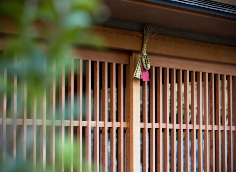 Traditional wooden lattice facade of a Kyoto machiya with a handwoven charm hanging at the entrance, capturing the quiet craft and cultural detail of Hotel New Awaji Group's Kyoto properties