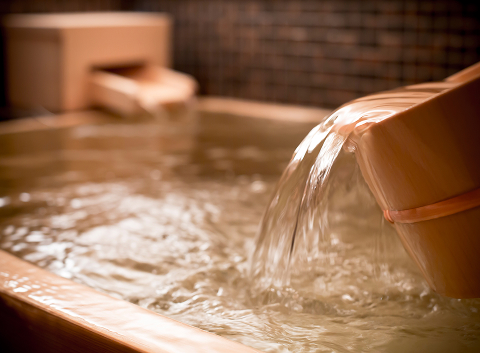 Warm water flowing into a wooden onsen bath, creating a calming and restorative wellness experience after a day in Kyoto