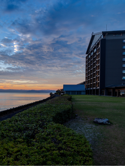 Hotel New Awaji Group's Lake Biwa property at dusk beneath a vivid blue and amber sky, with the lake's still waters stretching toward distant mountains