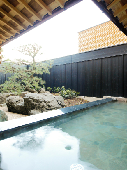 Private outdoor onsen with natural rock garden and wooden enclosure, creating a serene and sheltered bathing experience at Hotel New Awaji Group