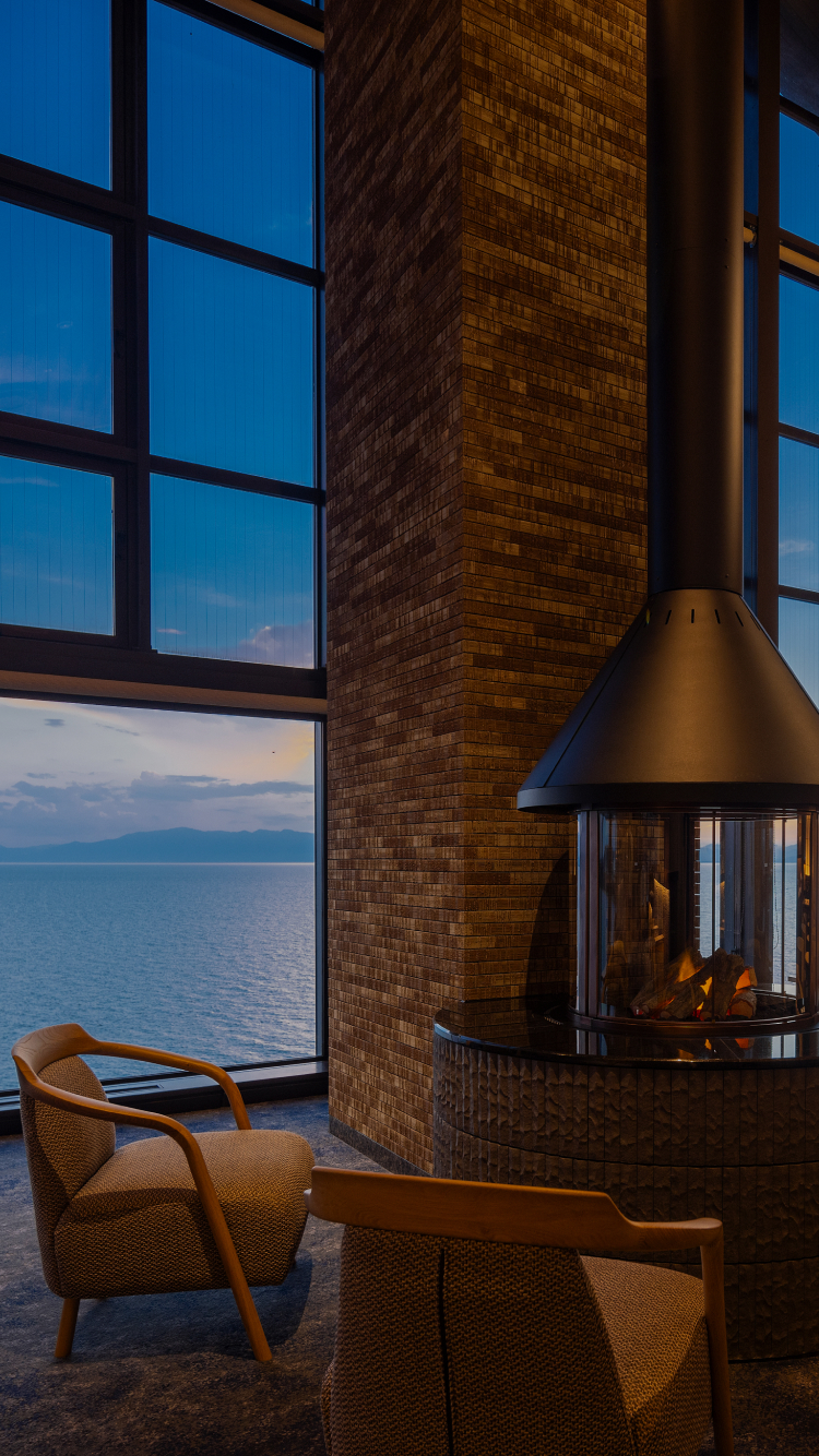 Sky Lounge at Hotel New Awaji Biwa Lake in Hikone, Shiga, Japan, featuring a central fireplace and floor-to-ceiling windows with panoramic views over Lake Biwa at dusk