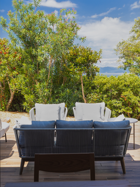 Private guest room terrace at Hotel New Awaji Lake Biwa with a woven lounge sofa, blue cushions, and a low table, framed by lush greenery with lake views beyond