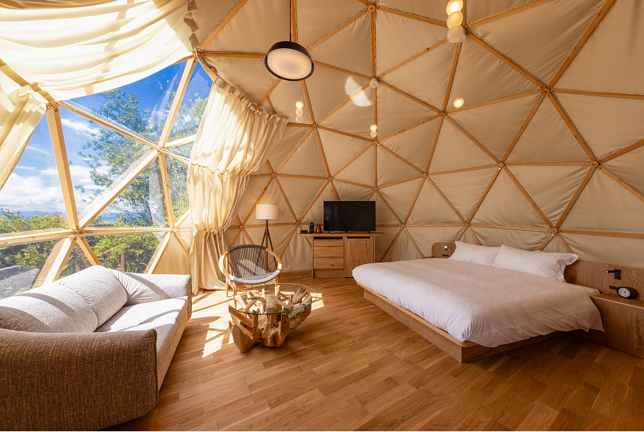 Spacious dome glamping suite with wood-frame ceiling, queen bed, lounge seating, and forest-view window at Hotel New Awaji Lake Biwa