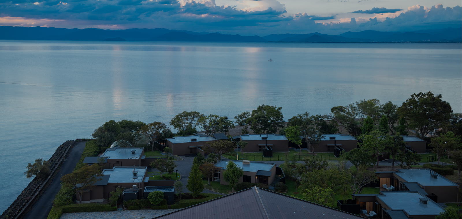 Aerial view of Hotel New Awaji Group's lakeside property at dusk, with calm Lake Biwa waters stretching toward distant mountains