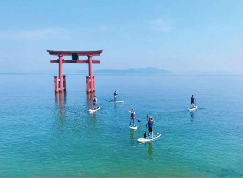 Guests paddleboarding on turquoise Lake Biwa waters near a traditional red torii gate, exploring the natural and cultural beauty of Japan's largest lake
