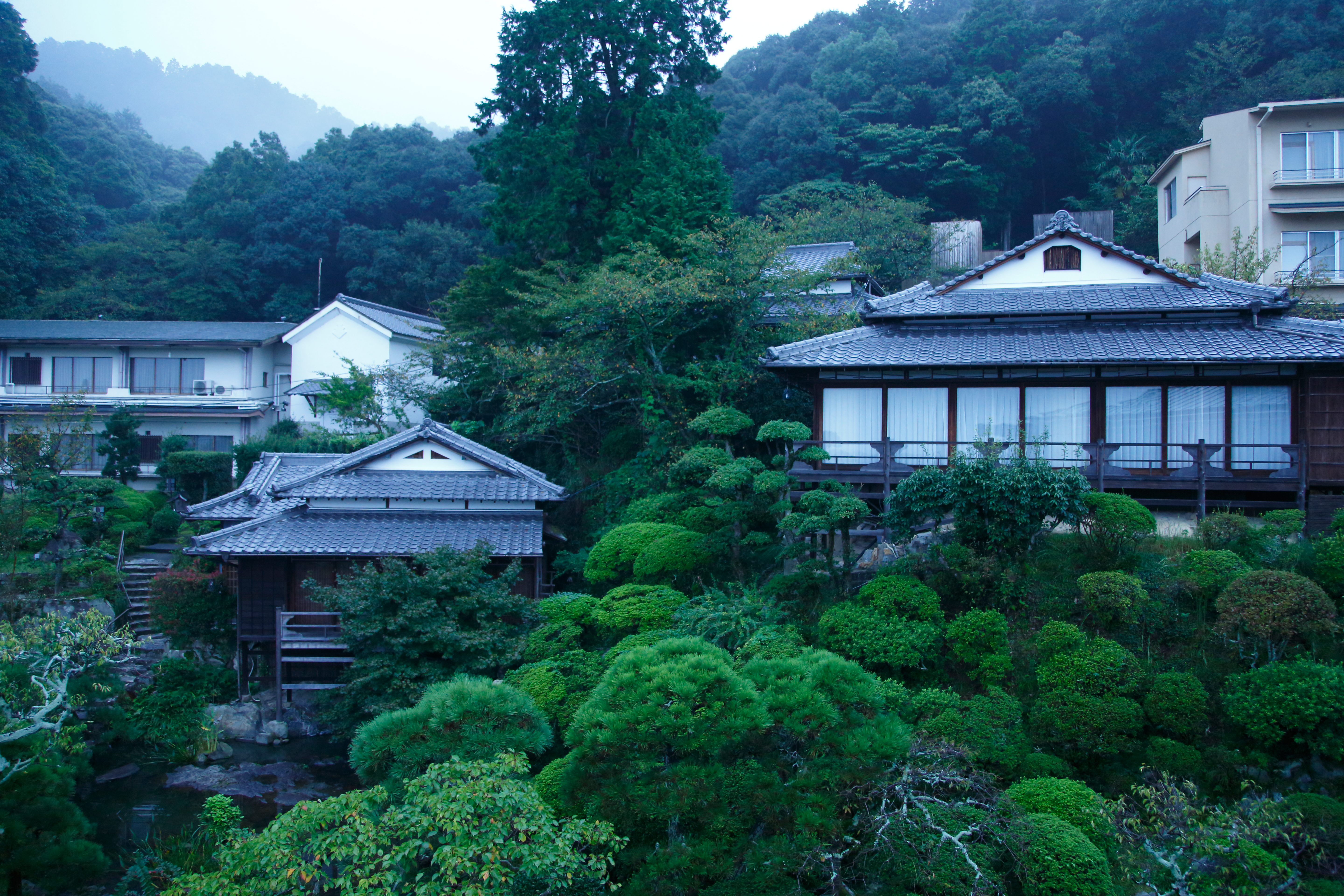 Traditional Japanese inn exterior with wooden verandas, stone lanterns, and manicured pine trees, embodying the quiet craftsmanship of a Shikoku ryokan stay