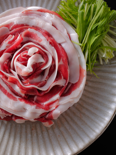 Regional pork or wagyu shabu-shabu slices arranged in a rose formation on ceramic, a signature of the artful and seasonal dining experience at Hotel New Awaji Group's Shikoku properties