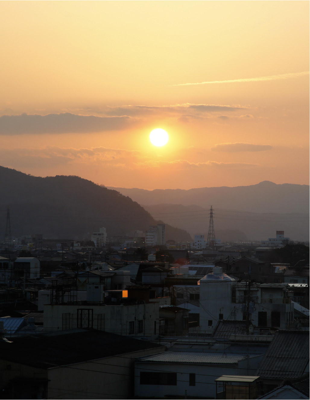 Golden sunset over Okayama city rooftops with mountain silhouettes on the horizon, marking the end of a day shaped by heritage, landscape, and restorative calm